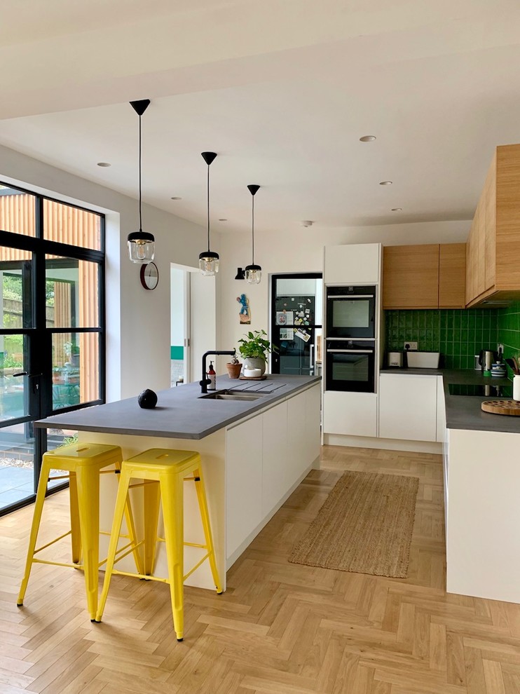 Design ideas for a contemporary u-shaped kitchen in West Midlands with flat-panel cabinets, white cabinets, green splashback, light hardwood floors, with island, beige floor and grey benchtop.