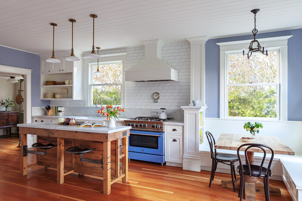 This is an example of a traditional single-wall eat-in kitchen in San Francisco with a farmhouse sink, open cabinets, white cabinets, marble benchtops, white splashback, subway tile splashback, coloured appliances, medium hardwood floors, with island and grey benchtop.