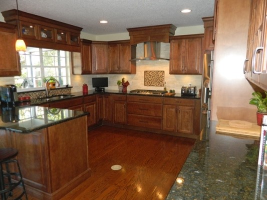 Photo of a large traditional u-shaped separate kitchen in Orlando with an undermount sink, raised-panel cabinets, medium wood cabinets, granite benchtops, beige splashback, stainless steel appliances, dark hardwood floors and a peninsula.