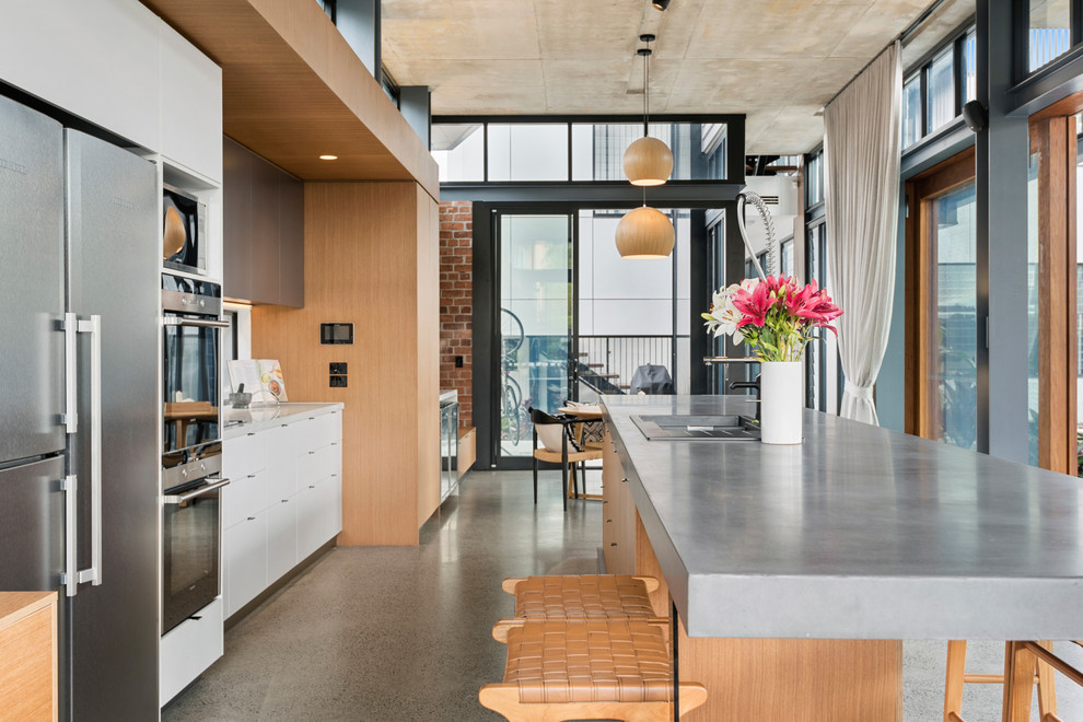 Inspiration for an expansive industrial galley open plan kitchen in Brisbane with concrete benchtops, concrete floors, with island, grey benchtop, flat-panel cabinets, white cabinets, stainless steel appliances and grey floor.