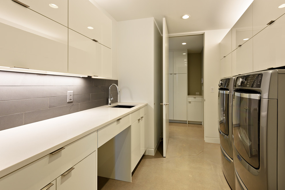 Inspiration for a mid-sized contemporary utility room in Salt Lake City with an undermount sink, flat-panel cabinets, white cabinets, quartz benchtops, grey walls, concrete floors, a side-by-side washer and dryer and beige floor.