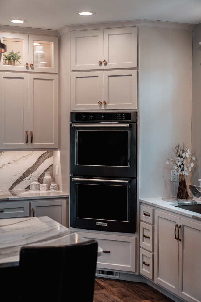 Large transitional l-shaped medium tone wood floor and brown floor open concept kitchen photo with an undermount sink, flat-panel cabinets, white cabinets, quartz countertops, multicolored backsplash, quartz backsplash, black appliances, an island and multicolored countertops