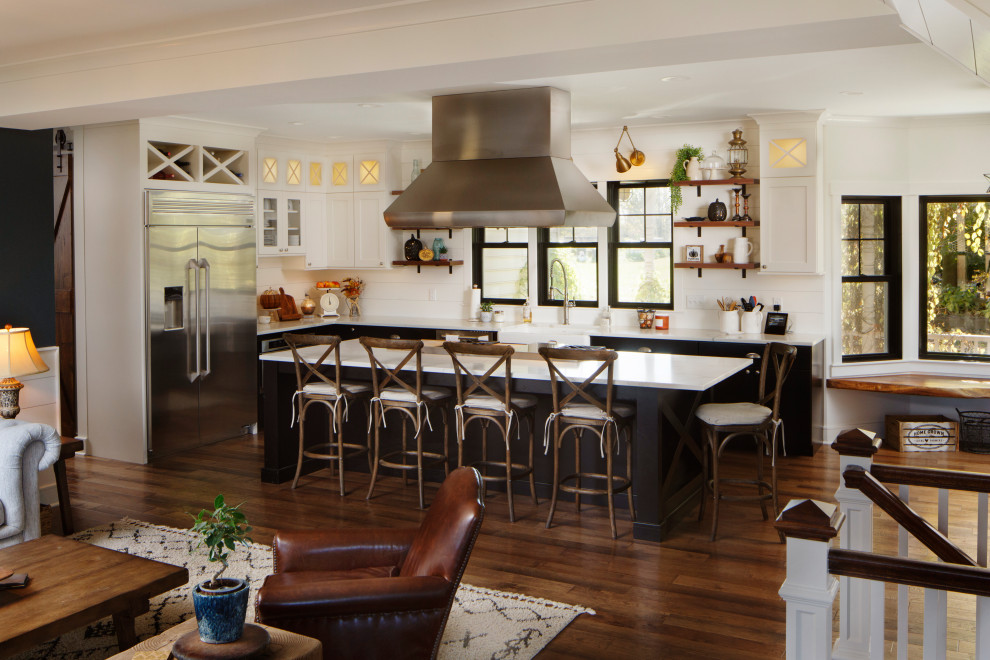 This is an example of a large country eat-in kitchen in Other with a farmhouse sink, shaker cabinets, black cabinets, quartz benchtops, white splashback, shiplap splashback, stainless steel appliances, medium hardwood floors, with island, brown floor and white benchtop.