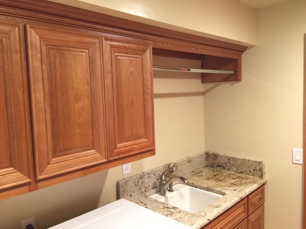 Inspiration for a galley laundry room in Other with an undermount sink, raised-panel cabinets, medium wood cabinets, granite benchtops, yellow walls, travertine floors and a side-by-side washer and dryer.