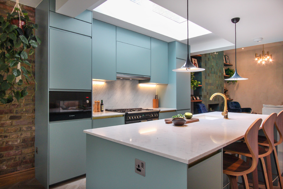 This is an example of a mid-sized contemporary galley open plan kitchen in London with a drop-in sink, recessed-panel cabinets, blue cabinets, quartzite benchtops, white splashback, marble splashback, light hardwood floors, white floor, panelled appliances, with island and white benchtop.