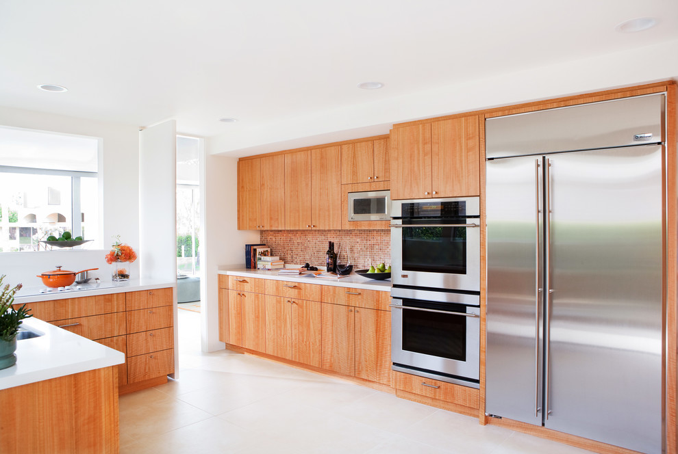 This is an example of a large contemporary u-shaped separate kitchen in Los Angeles with a drop-in sink, flat-panel cabinets, light wood cabinets, orange splashback, glass tile splashback, stainless steel appliances, quartz benchtops, ceramic floors, a peninsula and white floor.