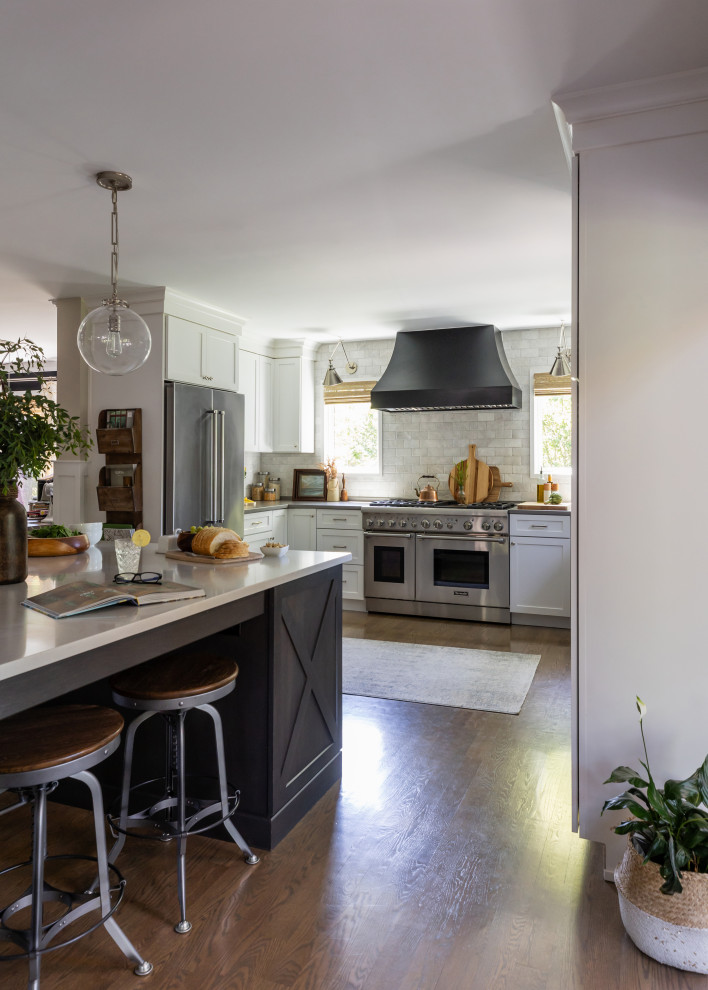 Example of a mid-sized transitional u-shaped medium tone wood floor and brown floor open concept kitchen design in Chicago with a farmhouse sink, shaker cabinets, white cabinets, quartz countertops, white backsplash, marble backsplash, stainless steel appliances, an island and gray countertops