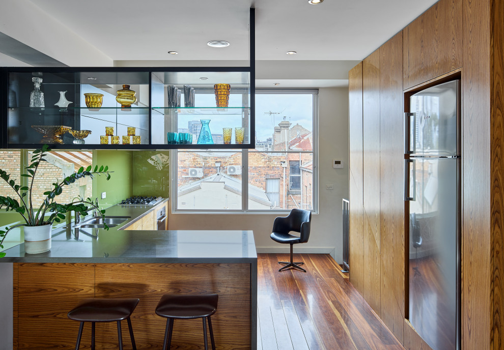 This is an example of a small midcentury l-shaped home bar in Melbourne with glass-front cabinets and solid surface benchtops.