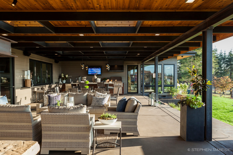 This is an example of an expansive contemporary backyard deck in Portland with an outdoor kitchen and a roof extension.