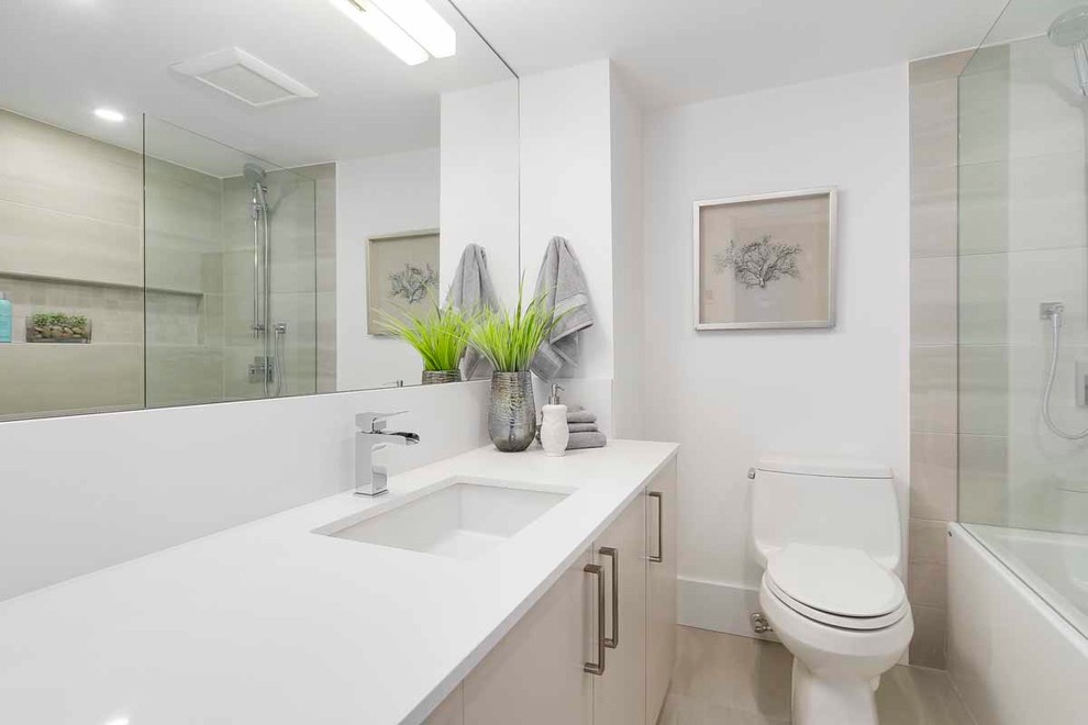 Photo of a small contemporary kids bathroom in Vancouver with flat-panel cabinets, grey cabinets, a drop-in tub, a shower/bathtub combo, a one-piece toilet, gray tile, porcelain tile, white walls, porcelain floors, an undermount sink, engineered quartz benchtops, grey floor and white benchtops.