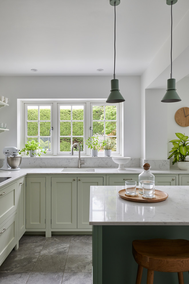This is an example of a medium sized classic l-shaped enclosed kitchen in London with a built-in sink, shaker cabinets, green cabinets, quartz worktops, grey splashback, engineered quartz splashback, stainless steel appliances, ceramic flooring, an island, grey floors, grey worktops and feature lighting.
