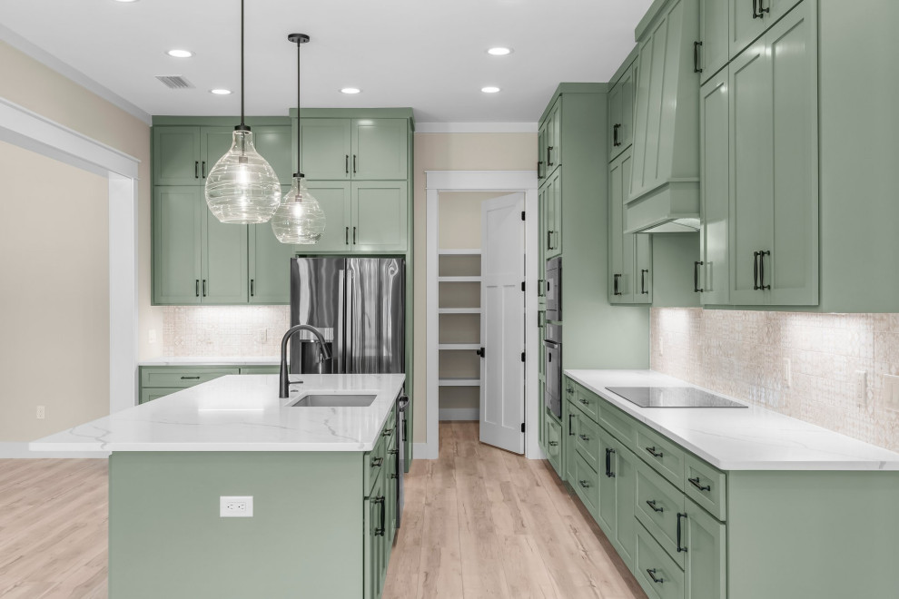 Example of an arts and crafts l-shaped vinyl floor and beige floor open concept kitchen design with an undermount sink, shaker cabinets, green cabinets, quartzite countertops, beige backsplash, porcelain backsplash, stainless steel appliances, an island and white countertops
