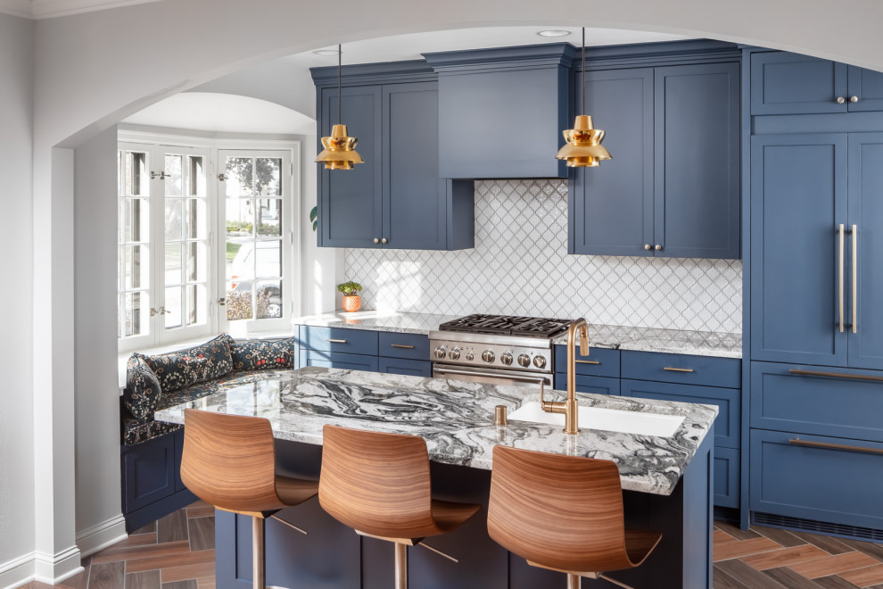 This is an example of a transitional galley kitchen in Minneapolis with an undermount sink, shaker cabinets, blue cabinets, white splashback, panelled appliances, with island, brown floor and grey benchtop.