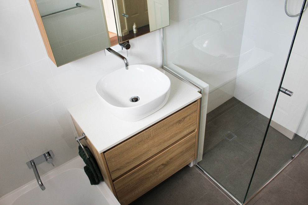 Design ideas for a small modern kids bathroom in Perth with flat-panel cabinets, dark wood cabinets, a drop-in tub, a corner shower, white tile, ceramic tile, white walls, porcelain floors, a vessel sink, engineered quartz benchtops, grey floor, a hinged shower door and white benchtops.