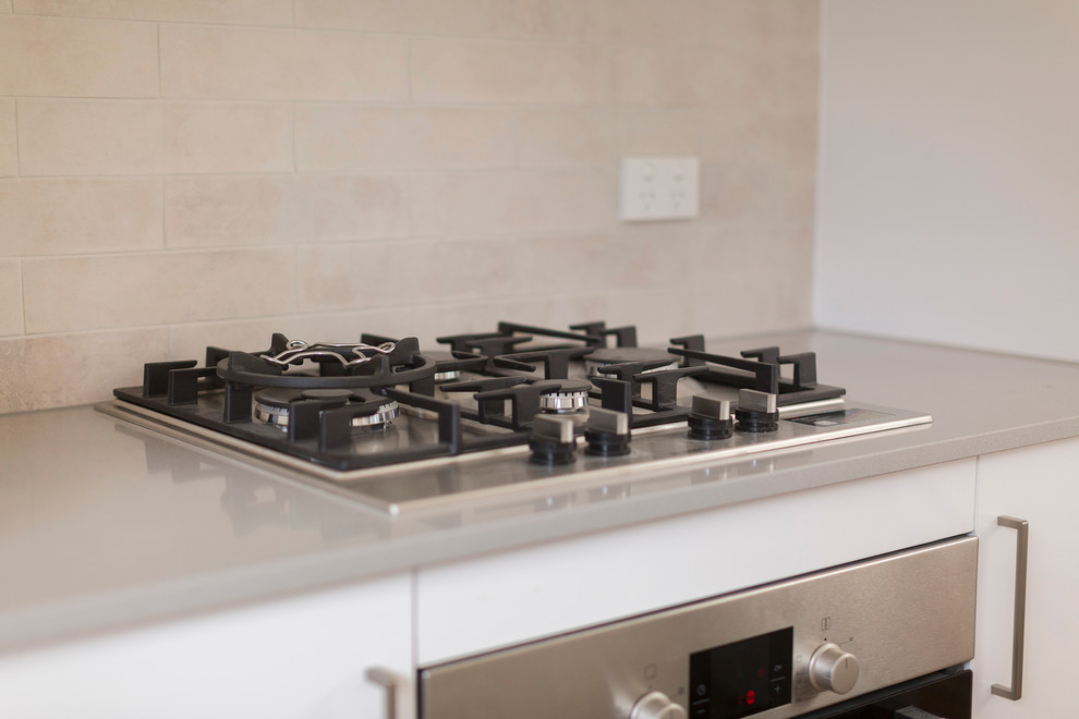 Photo of a small traditional galley eat-in kitchen in Canberra - Queanbeyan with a double-bowl sink, flat-panel cabinets, white cabinets, quartz benchtops, grey splashback, porcelain splashback, stainless steel appliances, vinyl floors, with island, brown floor and grey benchtop.