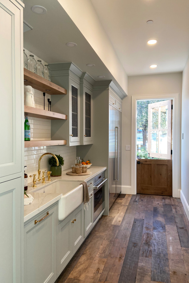 Inredning av ett lantligt stort grå grått kök, med en rustik diskho, skåp i shakerstil, blå skåp, bänkskiva i kvarts, vitt stänkskydd, stänkskydd i keramik, rostfria vitvaror, mellanmörkt trägolv och brunt golv