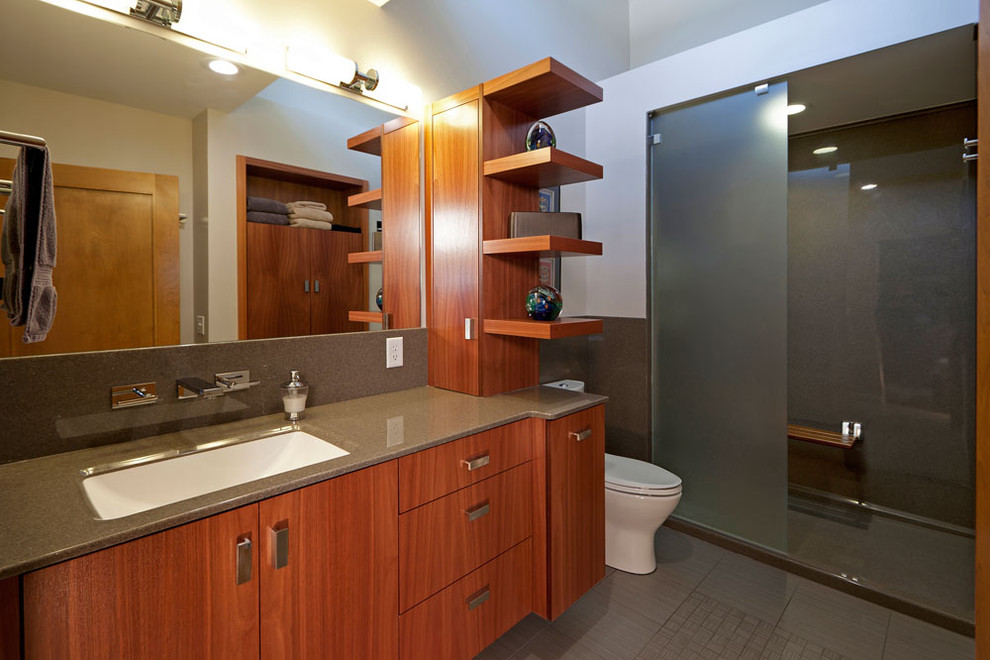 This is an example of a mid-sized modern master bathroom in St Louis with ceramic tile, an open shower, flat-panel cabinets, medium wood cabinets, a one-piece toilet, gray tile, white walls, porcelain floors, onyx benchtops, an undermount sink and an open shower.