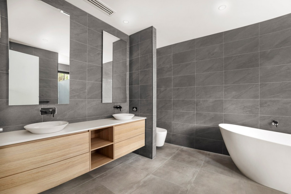 Design ideas for a modern master bathroom in Melbourne with flat-panel cabinets, light wood cabinets, a freestanding tub, an open shower, a wall-mount toilet, gray tile, porcelain tile, grey walls, porcelain floors, a vessel sink, quartzite benchtops, grey floor, an open shower, white benchtops, a double vanity and a floating vanity.