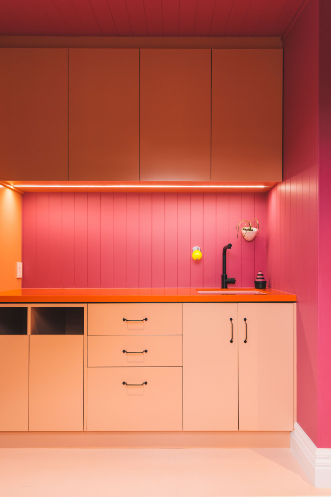 Design ideas for a contemporary galley laundry room in Other with an undermount sink, raised-panel cabinets, orange cabinets, laminate benchtops, pink splashback, timber splashback, pink walls, painted wood floors, a stacked washer and dryer, pink floor, orange benchtop, timber and decorative wall panelling.