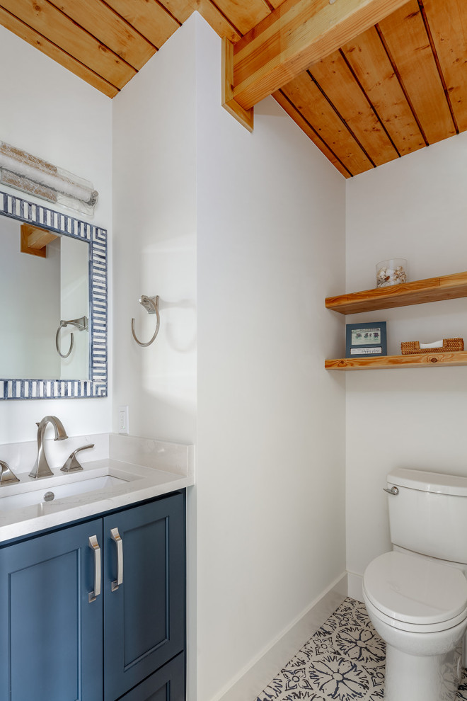 Small beach style powder room in Columbus with shaker cabinets, blue cabinets, a two-piece toilet, white walls, cement tiles, an undermount sink, engineered quartz benchtops, multi-coloured floor, white benchtops, a built-in vanity and timber.