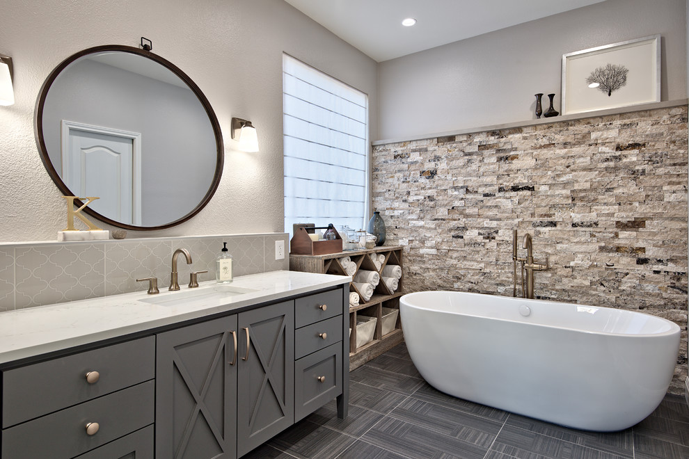 This is an example of a mid-sized transitional master bathroom in Austin with grey cabinets, a freestanding tub, a corner shower, gray tile, travertine, white walls, ceramic floors, an undermount sink, engineered quartz benchtops, grey floor and recessed-panel cabinets.