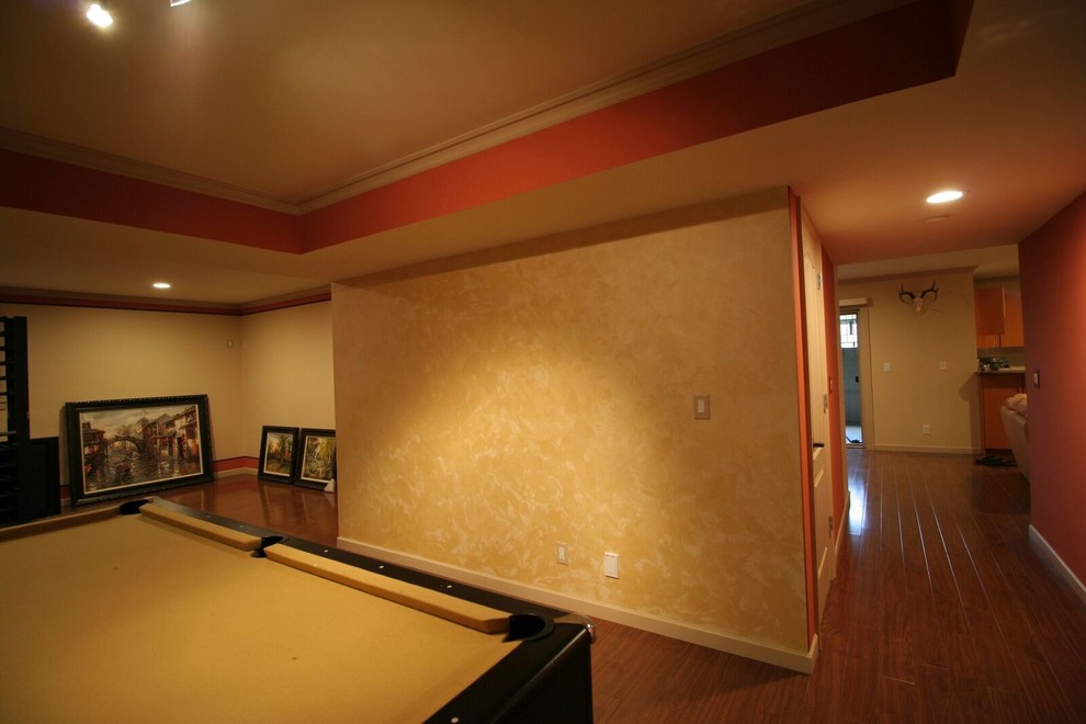Design ideas for a mid-sized transitional fully buried basement in Vancouver with orange walls, medium hardwood floors, a standard fireplace, a stone fireplace surround and brown floor.