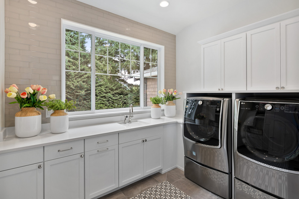 Large arts and crafts l-shaped dedicated laundry room in Seattle with an undermount sink, shaker cabinets, white cabinets, quartzite benchtops, grey splashback, glass tile splashback, white walls, ceramic floors, a side-by-side washer and dryer, grey floor and white benchtop.