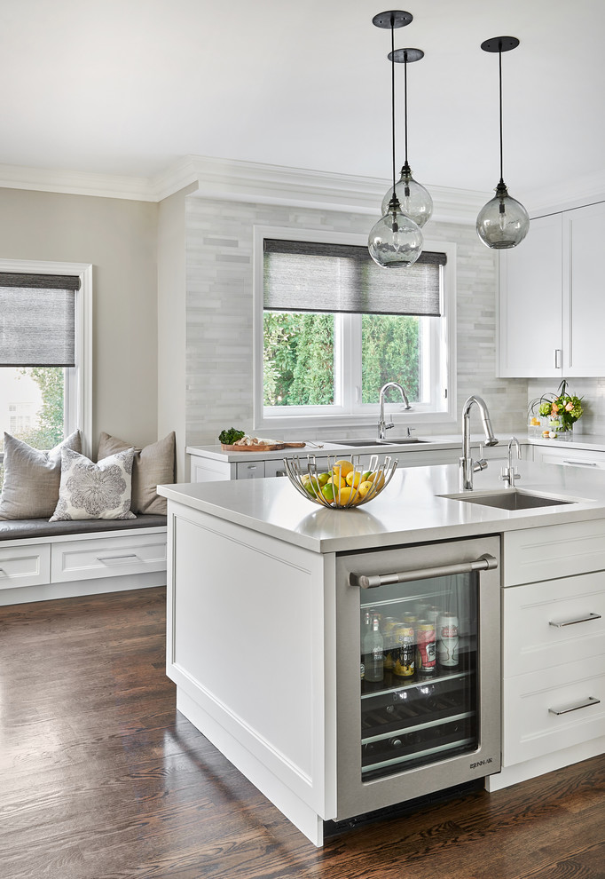 This is an example of a beach style kitchen in Toronto with an undermount sink, shaker cabinets, white cabinets, quartz benchtops, grey splashback, marble splashback, stainless steel appliances, dark hardwood floors, with island, brown floor and grey benchtop.