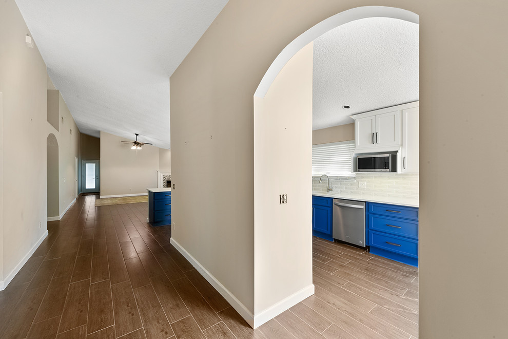 Open concept kitchen - large transitional l-shaped vinyl floor and brown floor open concept kitchen idea in Jacksonville with an undermount sink, shaker cabinets, blue cabinets, quartzite countertops, white backsplash, ceramic backsplash, stainless steel appliances and a peninsula