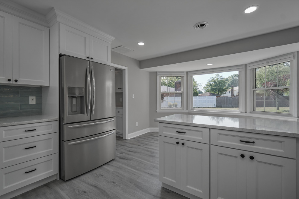 Foto på ett funkis vit kök med öppen planlösning, med en dubbel diskho, luckor med infälld panel, vita skåp, granitbänkskiva, blått stänkskydd, stänkskydd i glaskakel och laminatgolv