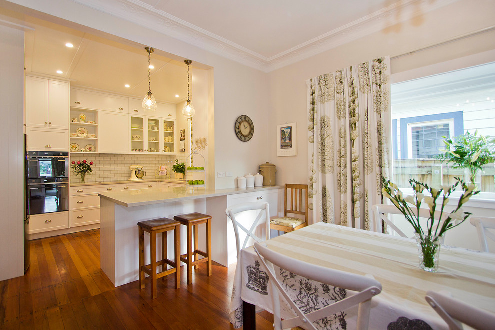 Inspiration for a small traditional u-shaped eat-in kitchen in Wellington with an undermount sink, shaker cabinets, white cabinets, granite benchtops, white splashback, subway tile splashback, stainless steel appliances, medium hardwood floors and a peninsula.