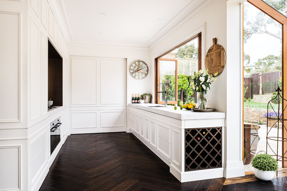 Photo of a large traditional u-shaped separate kitchen in Melbourne with an undermount sink, raised-panel cabinets, white cabinets, marble benchtops, white splashback, marble splashback, black appliances, dark hardwood floors, no island and brown floor.