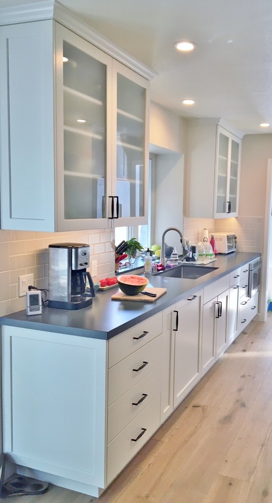 Inspiration for a mid-sized country galley separate kitchen in San Francisco with an undermount sink, shaker cabinets, white cabinets, quartz benchtops, grey splashback, ceramic splashback, stainless steel appliances, light hardwood floors, yellow floor and grey benchtop.