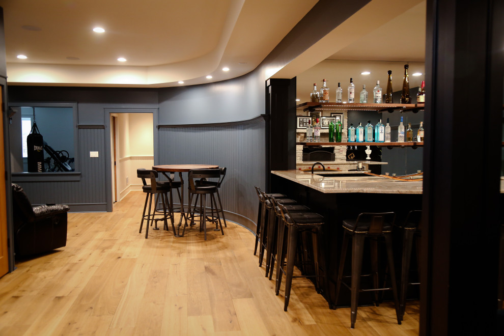 Aménagement d'un grand sous-sol classique enterré avec un bar de salon, un mur bleu, parquet clair, une cheminée standard et un manteau de cheminée en pierre.
