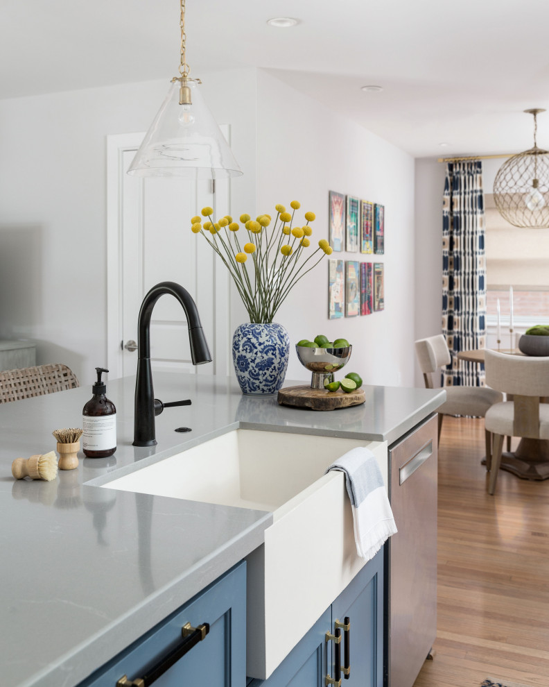 This is an example of a mid-sized eclectic galley open plan kitchen in Houston with a farmhouse sink, shaker cabinets, blue cabinets, quartz benchtops, multi-coloured splashback, marble splashback, stainless steel appliances, light hardwood floors, with island and grey benchtop.