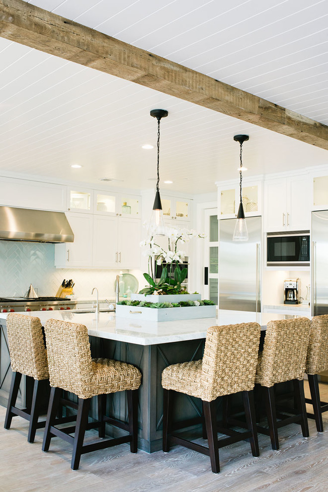 This is an example of a beach style kitchen in Los Angeles with shaker cabinets, white cabinets, white splashback, ceramic splashback, stainless steel appliances, light hardwood floors and with island.