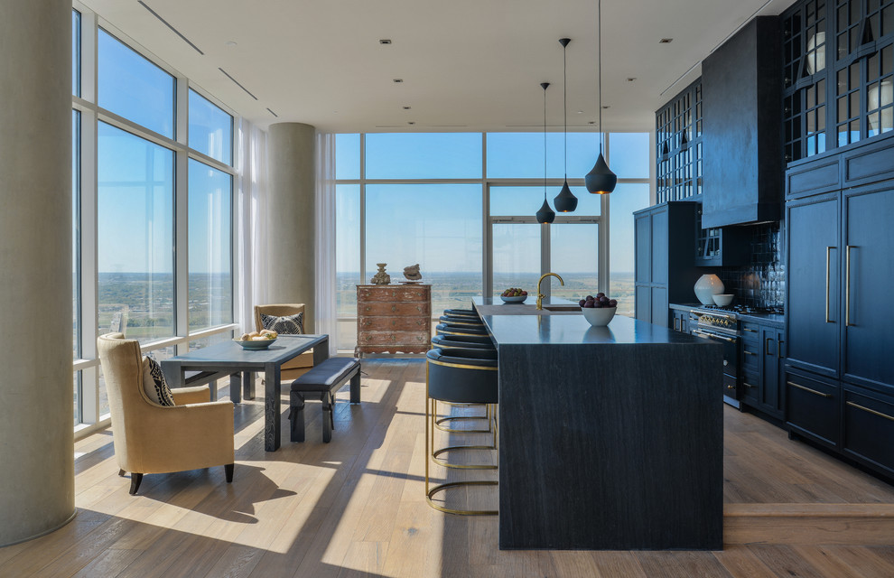 Open concept kitchen - mid-sized contemporary single-wall light wood floor and beige floor open concept kitchen idea in Orange County with glass-front cabinets, black cabinets, black backsplash, paneled appliances, an island, a farmhouse sink, solid surface countertops and ceramic backsplash