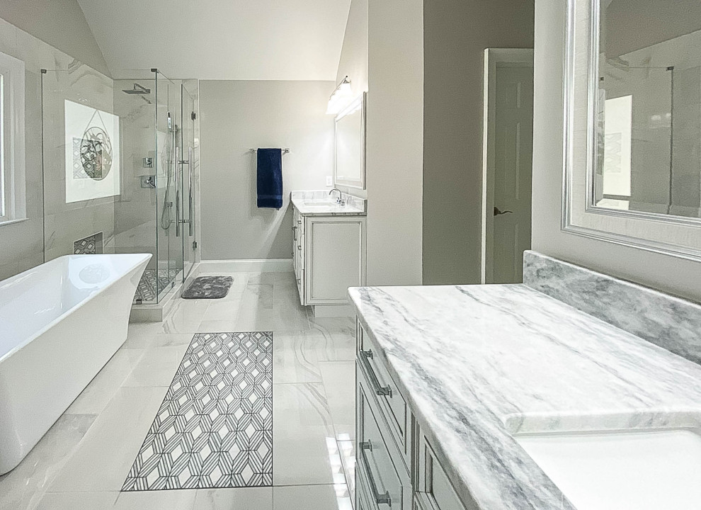 This is an example of an expansive contemporary master bathroom in Atlanta with recessed-panel cabinets, white cabinets, a freestanding tub, a two-piece toilet, white tile, porcelain tile, grey walls, porcelain floors, an undermount sink, marble benchtops, grey floor, a hinged shower door, grey benchtops, a niche, a double vanity and a built-in vanity.