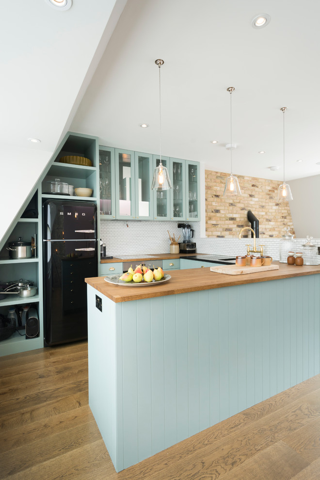 Design ideas for a small country u-shaped kitchen in London with an undermount sink, glass-front cabinets, blue cabinets, wood benchtops, white splashback, black appliances, medium hardwood floors and a peninsula.