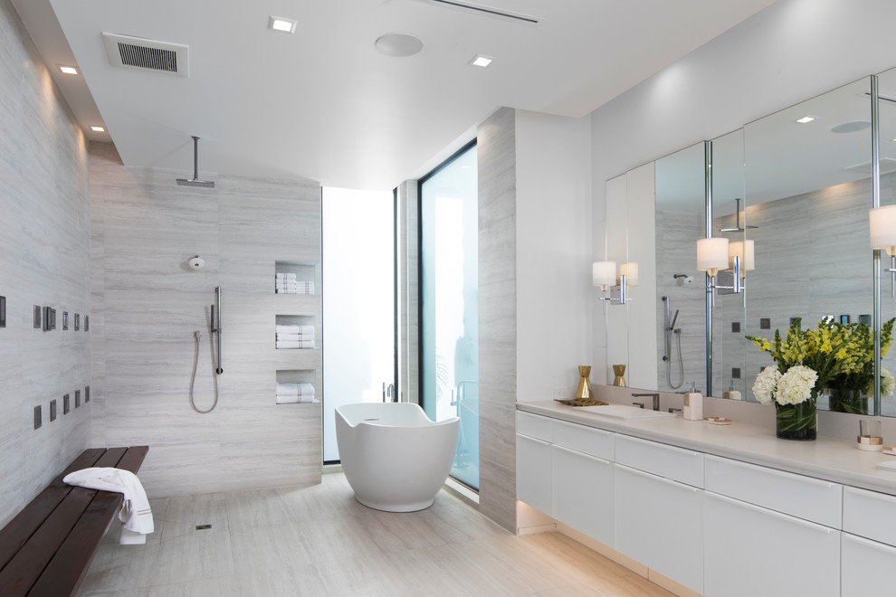 Expansive contemporary master bathroom in Orlando with flat-panel cabinets, white cabinets, a freestanding tub, an open shower, a wall-mount toilet, gray tile, grey walls, a drop-in sink and marble benchtops.