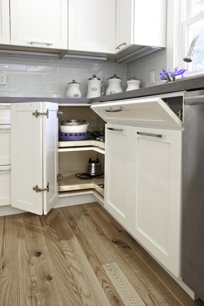 Example of a mid-sized transitional l-shaped medium tone wood floor eat-in kitchen design with flat-panel cabinets, white cabinets, stainless steel appliances, white walls, an island and solid surface countertops