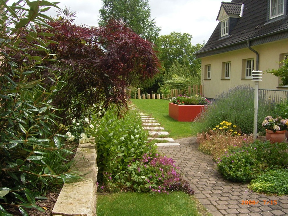 Garten im Sommer, neben dem Haus mit Hochbeet, direkter Sonneneinstrahlung und Natursteinplatten