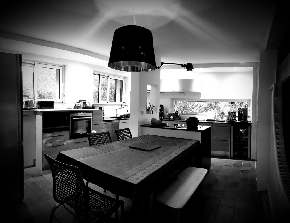 Cette image montre cuisine ouverte in L and bois clair With un évier encastré, un placard à porte affleurante, un plan de travail en granite, une crédence blanche, une crédence en feuille de verre, un électroménager en acier inoxydable, îlot, plan de travail noir and un plafond à caissons.