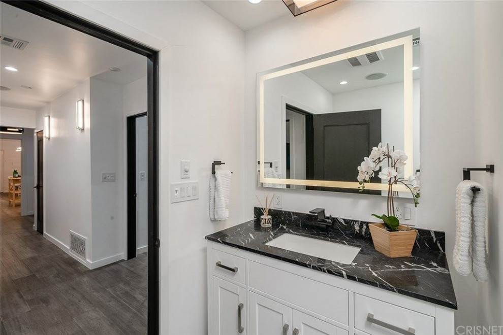 This is an example of a mid-sized modern master bathroom in Los Angeles with shaker cabinets, white cabinets, an alcove shower, a one-piece toilet, white walls, marble floors, an integrated sink, marble benchtops, white floor, a hinged shower door, black benchtops, a shower seat and a single vanity.
