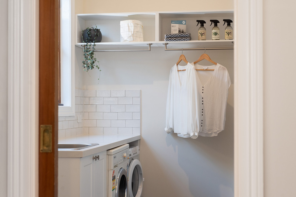 Design ideas for a mid-sized traditional galley utility room in Melbourne with a single-bowl sink, recessed-panel cabinets, white cabinets, quartz benchtops, white splashback, subway tile splashback, white walls, a side-by-side washer and dryer and white benchtop.