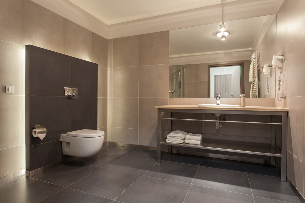 Photo of a contemporary bathroom in New York with a drop-in sink, a wall-mount toilet, beige tile and porcelain tile.