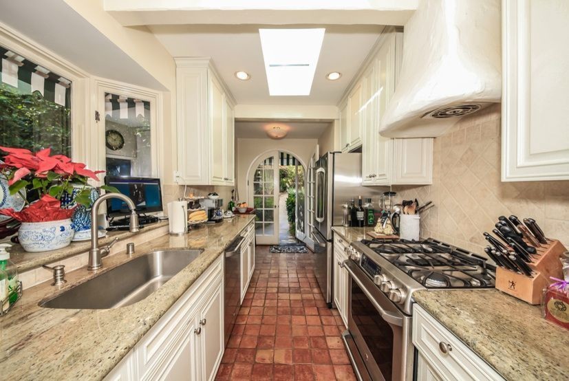 Mid-sized transitional u-shaped separate kitchen in Los Angeles with an undermount sink, raised-panel cabinets, white cabinets, limestone benchtops, beige splashback, ceramic splashback, stainless steel appliances, terra-cotta floors, no island and brown floor.