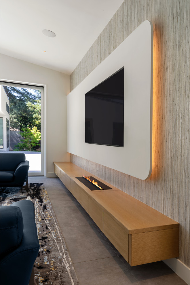 Example of a large minimalist open concept ceramic tile, gray floor, vaulted ceiling and wallpaper living room design in San Francisco with a bar, white walls, a ribbon fireplace, a wood fireplace surround and a media wall
