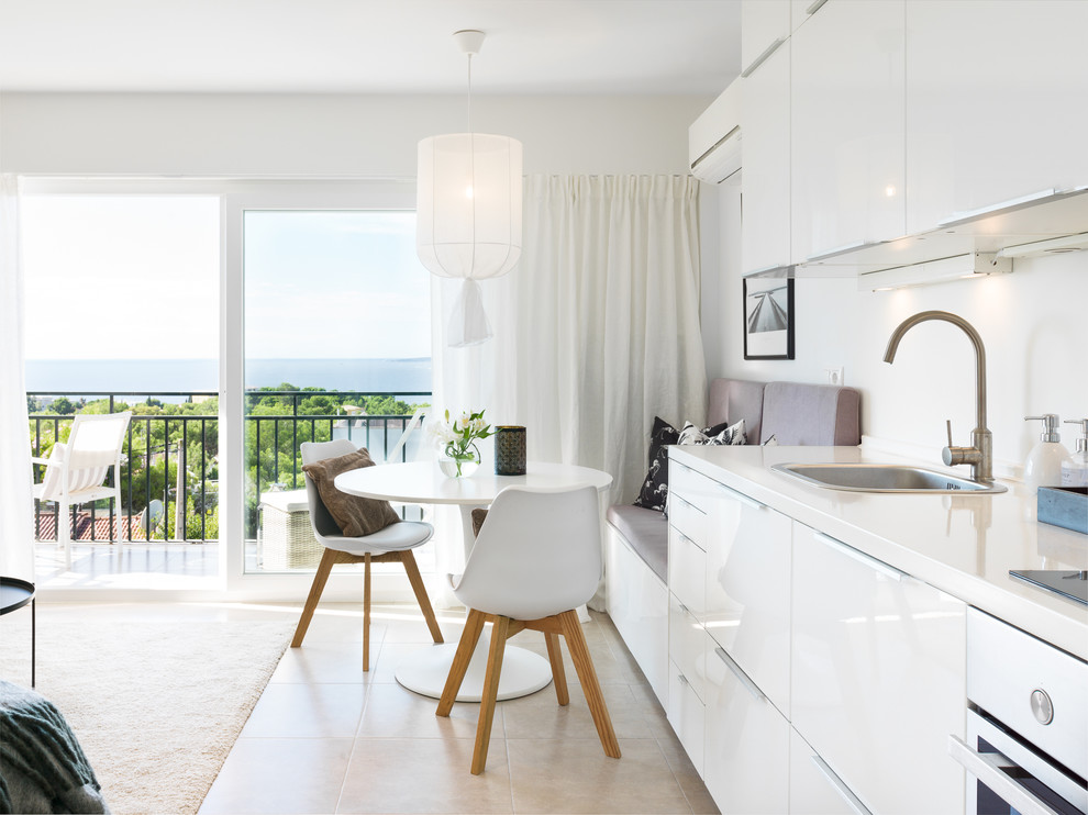 Inspiration for a mid-sized beach style single-wall open plan kitchen in Palma de Mallorca with flat-panel cabinets, white cabinets, white splashback, white appliances, ceramic floors, no island, beige floor, white benchtop and a drop-in sink.