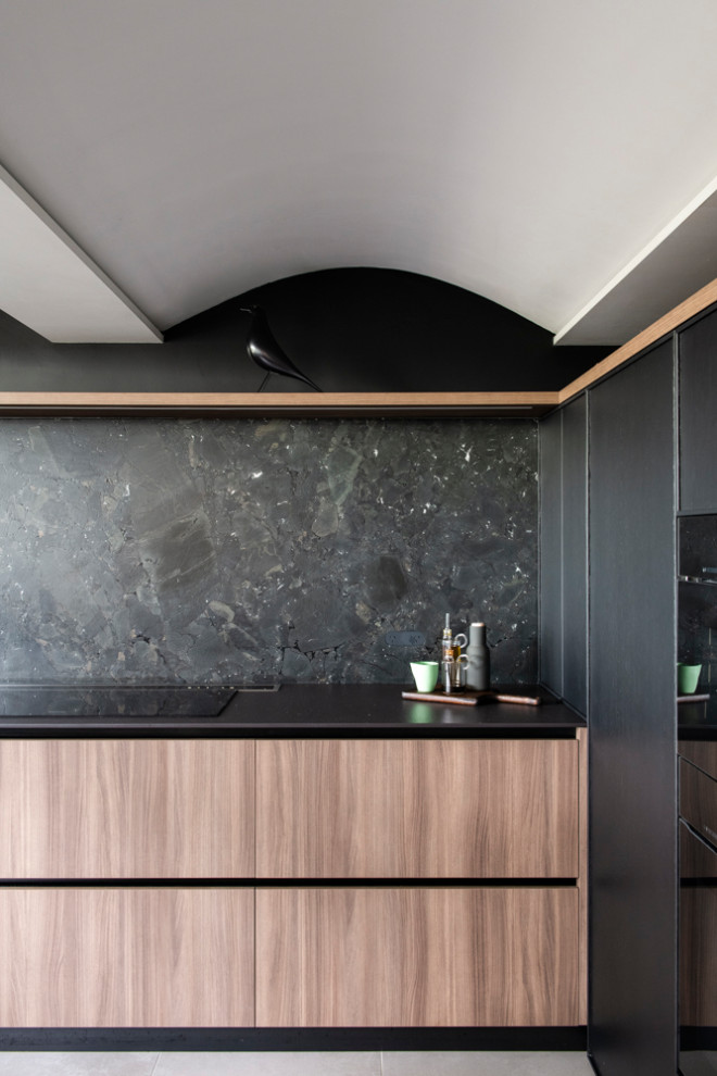 This is an example of a mid-sized modern u-shaped open plan kitchen in Sydney with an undermount sink, recessed-panel cabinets, black splashback, stone slab splashback, black appliances, porcelain floors, with island, black benchtop and wood.